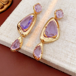 Detailed shot of vintage gold earrings with irregular purple gemstones on linen fabric