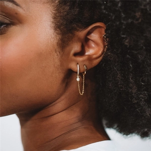 Macro detail of gold star earrings with delicate chain connecting double ear piercings