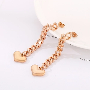 Detail shot of rose gold curb chain earrings with heart pendants on a white porcelain dish
