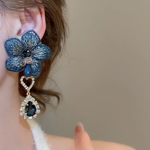 Dettaglio di orecchini a fiore ricamati blu con cristallo a goccia indossati