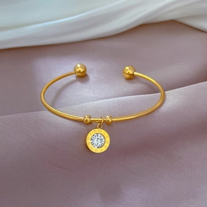 Detail of gold titanium steel bangle with Roman numeral charm and white zircon on silk
