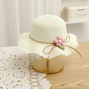 Detail of cream straw hat with floral accent and bow on a gold display stand