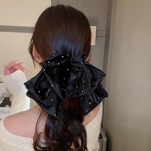 Détail d'un grand nœud à cheveux en velours noir avec cristaux sur cheveux bruns ondulés