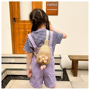 Rear view of a child wearing a beige woven crossbody bag with pink flower charm