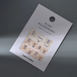 Close-up of MJ-065 gold nail charms with light blue rhinestones on display card