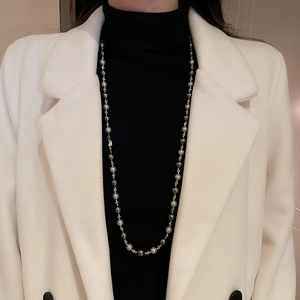 Détail d'un long collier de perles grises sur un pull noir et manteau beige