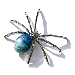 Macro shot of a silver spider ornament with a polished blue-green gemstone abdomen