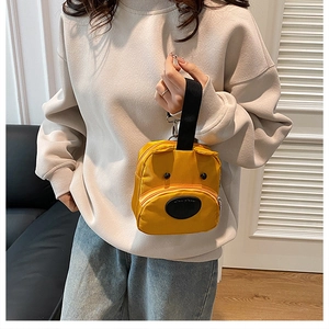Detalle de mini bolso amarillo con diseño de oso, correa negra y gancho metálico