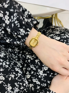 Detailed view of women's gold rectangular watch with stylish metal chain bracelet on wrist