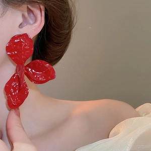 Close-up of a model wearing a large red 3-petal flower earring with matte texture