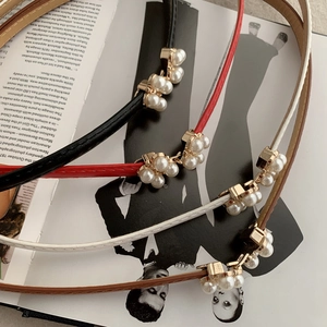 Detail of slim leather belt featuring five white pearls on a stylish magazine background