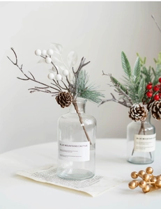 Close-up of artificial pine needles, red berries, and cones in a glass vase