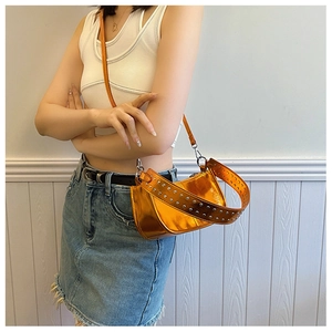 Detail of bright orange metallic shoulder bag featuring double-row silver studs on wide strap
