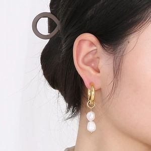 Détail de boucles d'oreilles créoles dorées avec doubles perles blanches