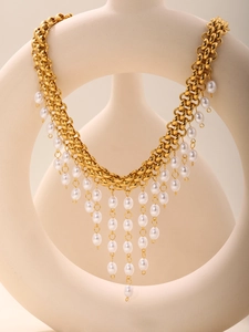 Détail d'un collier multicouche doré avec glands en perles blanches sur un buste minimaliste