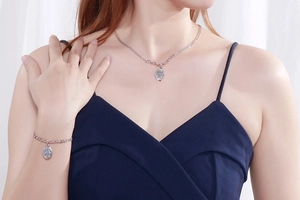 Silver necklace and bracelet set featuring oval embossed queen coin pendants on a model