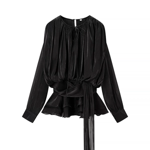 Détail d'un haut en satin noir à manches longues avec ceinture et ourlet volanté