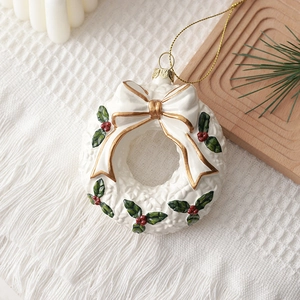 Cream white Christmas wreath ornament with gold bow and holly leaf decor on knit blanket