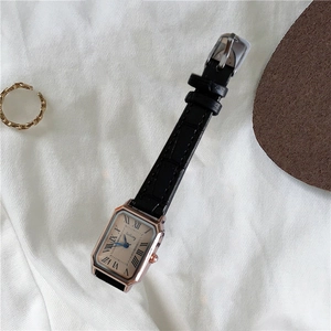 Detail view of square rose gold watch with black leather strap and Roman numerals on dial