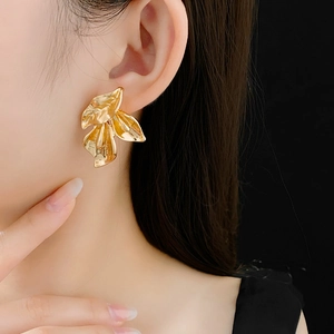 Gros plan de boucles d'oreilles pétales dorées portées sur un fond sombre