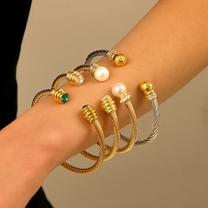 Two-tone cable wire bangle set with pearls and emerald charms on a female wrist