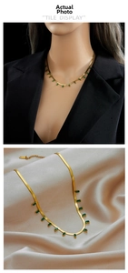 Detail of gold snake chain necklace with emerald green zircon stones on beige silk