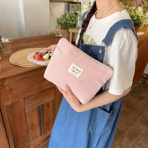 Close-up of pink corduroy makeup bag with label detail held by hand in soft light