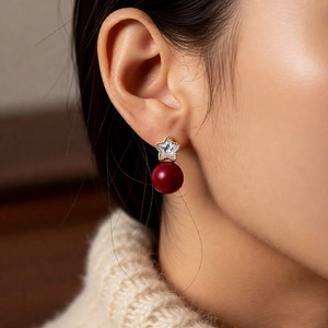Macro detail of star-shaped gold earring with crystal and round red pearl bead charm