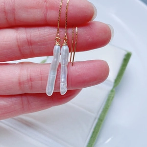 Detailed view of baroque pearl drop earrings with elegant golden chains held by hand