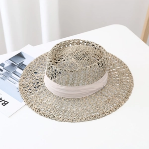 Detail of hand-woven seagrass sun hat with elegant beige ribbon on a minimal white surface