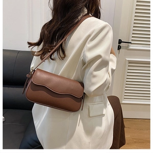 Detail of a brown leather crossbody bag with wave flap design and matching shoulder strap