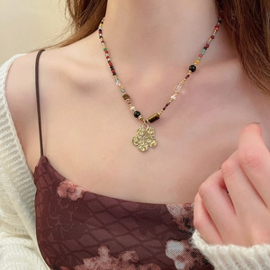 Detailed close-up of a handmade necklace with multi-colored beads and golden flower pendant