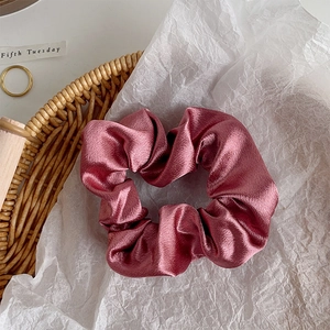 Detail of dusty pink satin scrunchie with soft pleats and elegant glossy finish