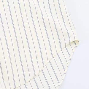 Close-up of curved hem and stitching detail on beige and blue striped cotton shirt