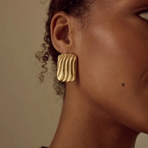 Gros plan de boucles d'oreilles dorées rectangulaires texturées portées par un mannequin