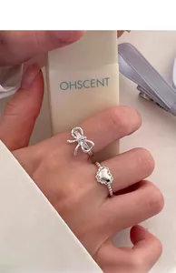 Detailed view of sterling silver bow and heart rings worn on fingers with a soft aesthetic