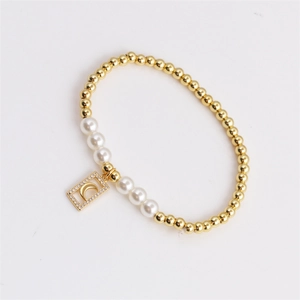 Dettaglio di un bracciale elastico con perline dorate, perle bianche e ciondolo luna