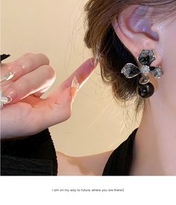 Detailed close-up of asymmetrical crystal flower earrings with elegant black pearl drop