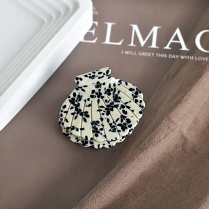 Detailed close-up of shell-shaped acetate hair claw clip with black ink splatters on cream