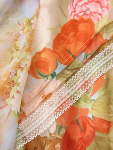 Close-up of floral chiffon fabric with orange rose patterns and white lace trim