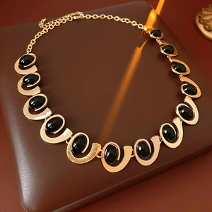 Détail du collier géométrique doré orné de pierres noires ovales sur fond de cuir marron