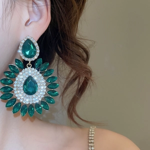 Close-up of sparkling emerald green waterdrop earrings with gold setting on model