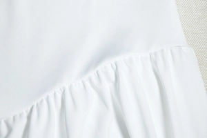 Dettaglio ravvicinato del tessuto bianco del vestito con trama fine e cuciture a pieghe