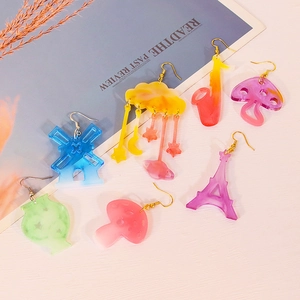 DIY resin earrings in mushroom, cloud, and saxophone shapes with gold hooks on a desk
