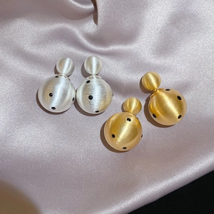 Detail of matte gold and silver double-bead earrings with black polka dots on silk
