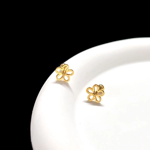 Macro detail of golden flower stud earrings on white ceramic edge with high-gloss finish