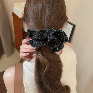 Close-up of black fabric scrunchie with white patterns on a low ponytail hair style