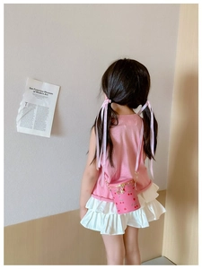 Rear view of a pink cherry print cylinder bag with a gold chain on a girl in a pleated skirt