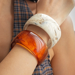 Close-up of wide marble white and amber resin bangles set on wrist for women