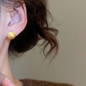 Close-up of minimalist matte gold round stud earrings worn on a model's earlobe